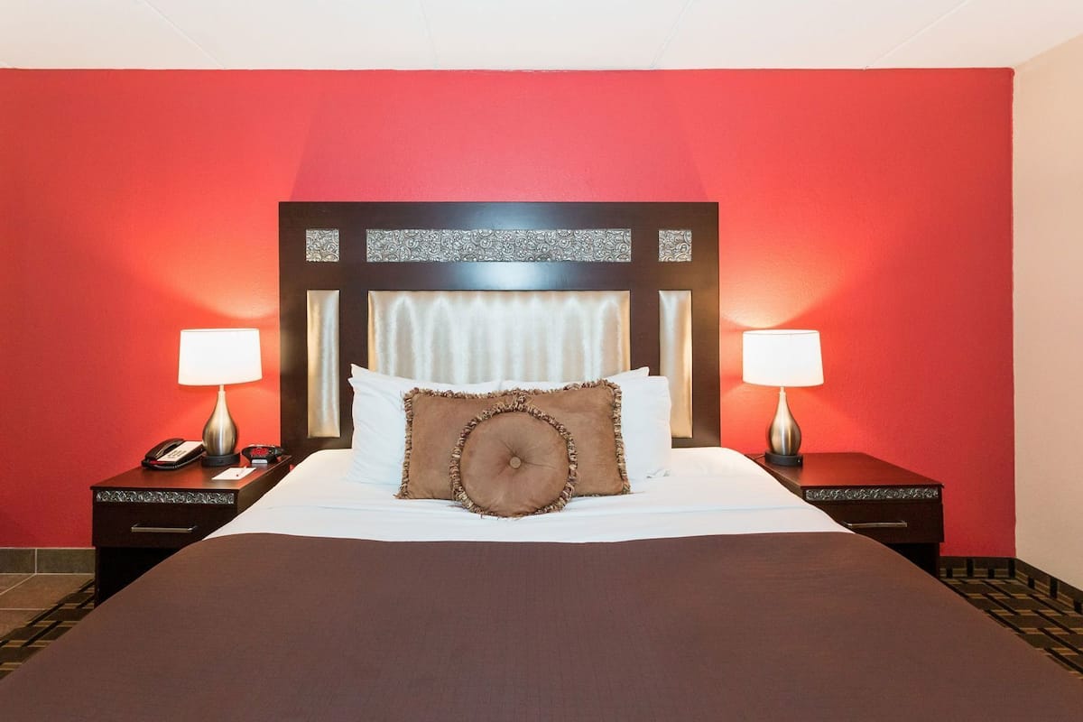 Une chambre d’hôtel avec un grand lit, deux tables de chevet avec des lampes, un téléphone et une tête de lit décorative.