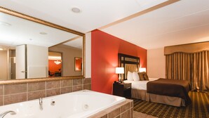 A hotel room with a large white bathtub, a bed with a brown headboard, and a red accent wall. - Ramada Hotel & Conference Center by Wyndham Plymouth (Plymouth)