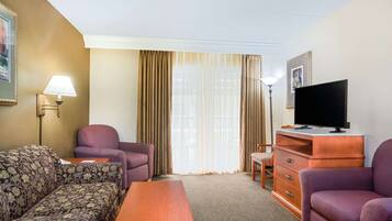 Habitación de hotel con sofá, sillón, televisión y una pequeña mesa.