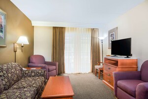 Habitación de hotel con sofá, sillón, televisión y una pequeña mesa.