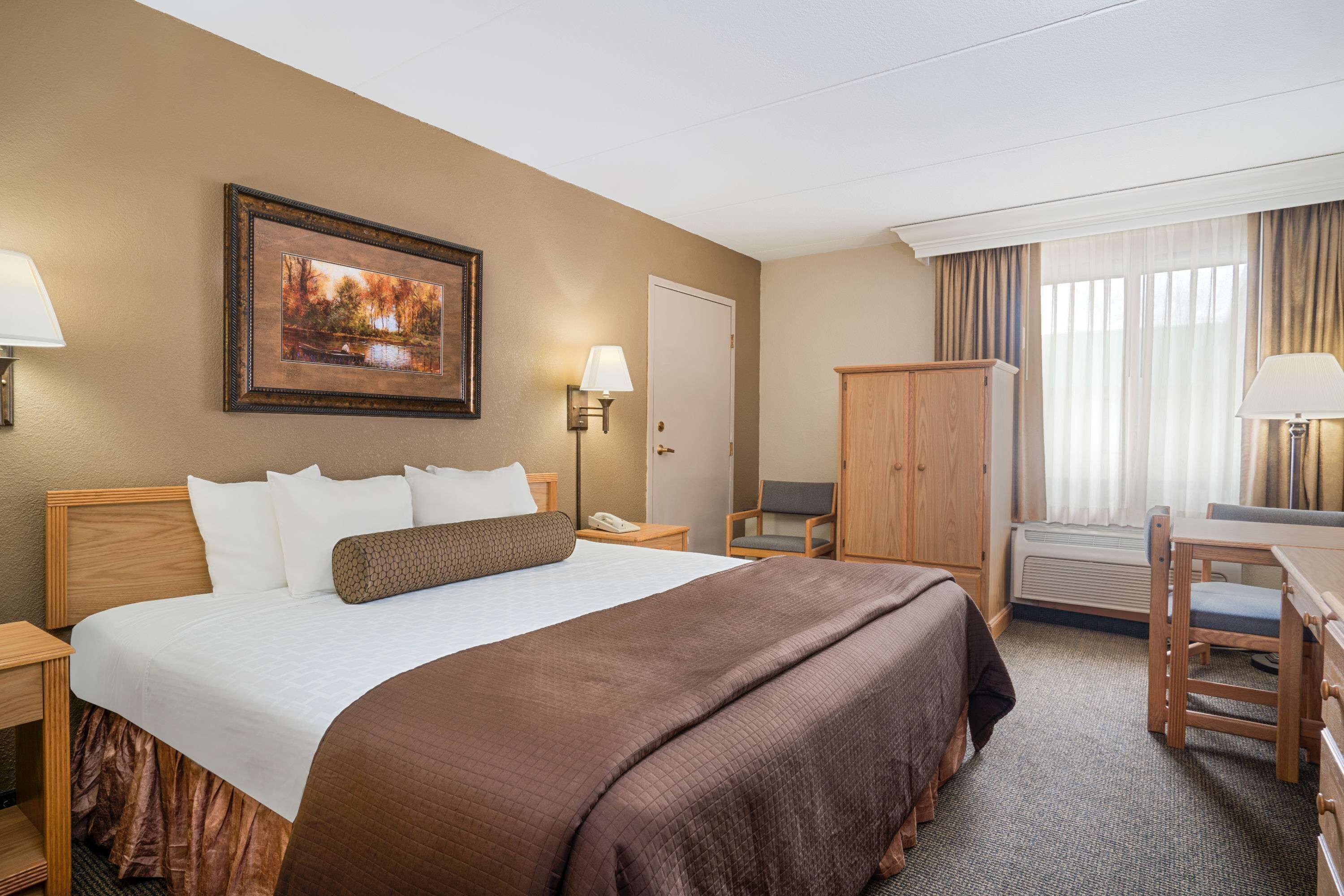 Una habitación de hotel con una cama grande, un escritorio, una silla, un armario y un cuadro en la pared.