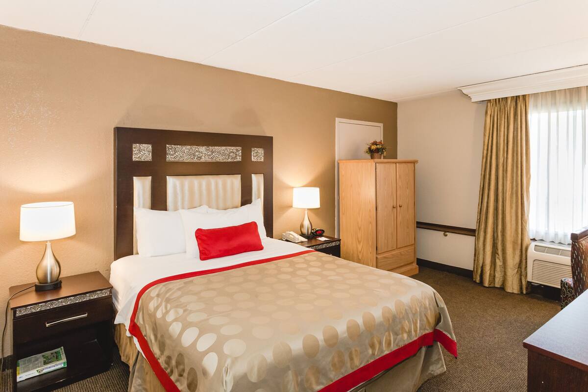 Une chambre d’hôtel avec un grand lit, deux tables de chevet avec des lampes, une armoire en bois et une fenêtre avec des rideaux.