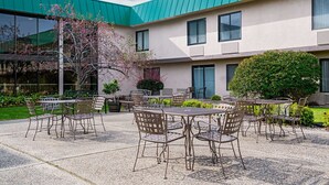 An outdoor patio with tables and chairs, a building with a green roof, and a small garden area. - Ramada Hotel & Conference Center by Wyndham Plymouth (Plymouth)