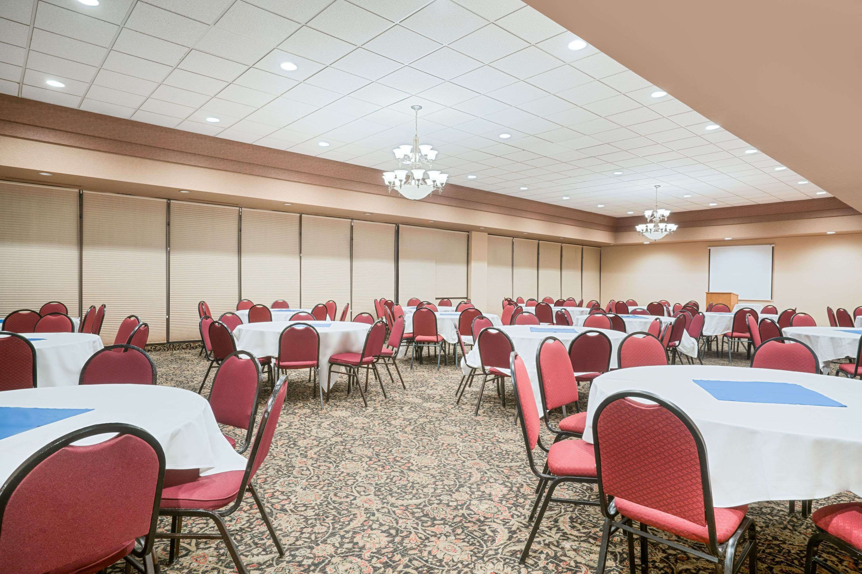 Un salón de conferencias con filas de mesas y sillas, piso alfombrado y un candelabro.