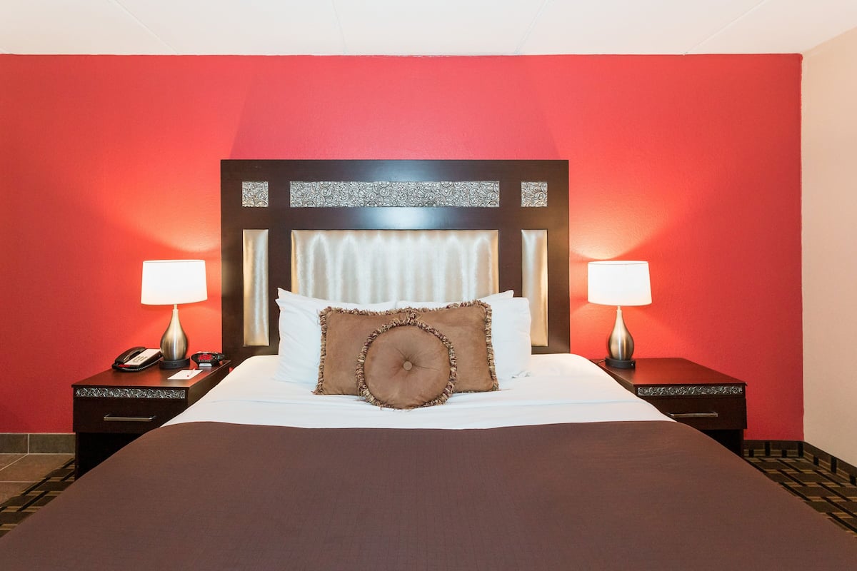 Une chambre d’hôtel avec un grand lit, deux tables de chevet avec des lampes et un mur rouge.