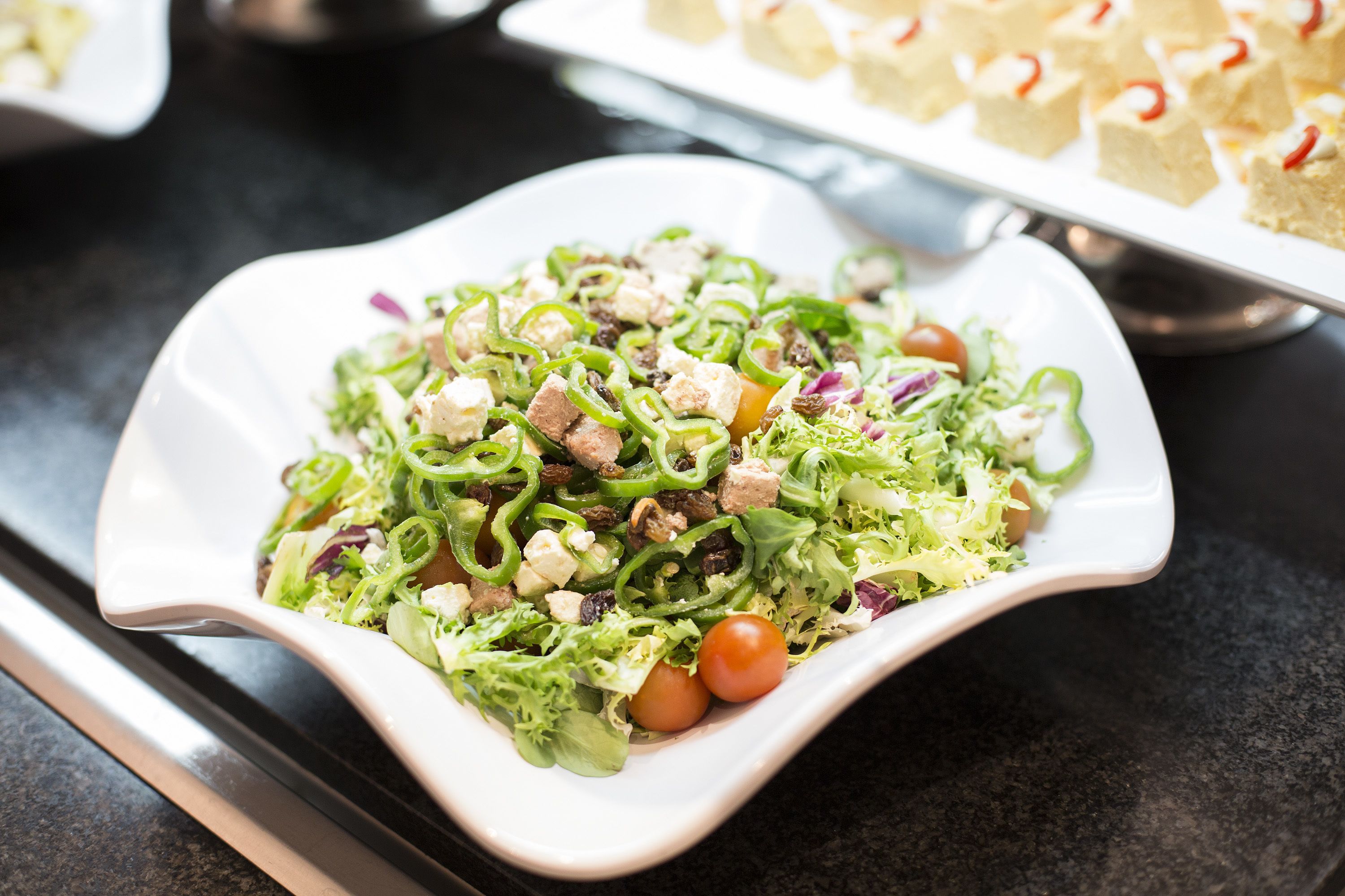 A white, square-shaped plate with a salad containing green peppers, tomatoes, and other vegetables.