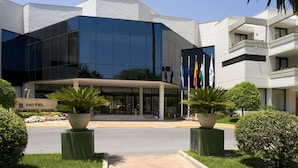 Un hotel moderno con fachada de vidrio, una entrada central y un jardín bien cuidado.
