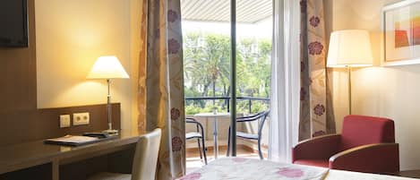 A hotel room with a bed, desk, chair, and a balcony with a table and chairs.