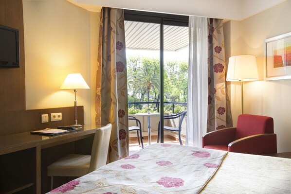 Habitación de hotel con cama, escritorio, silla y balcón con mesa y sillas.