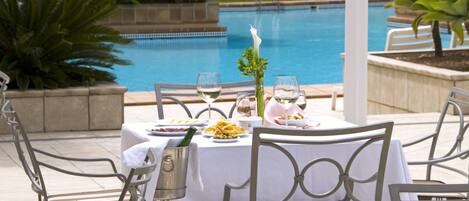 A dining table set outdoors with a pool in the background.