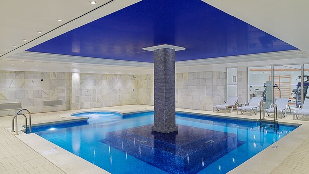 Una piscina interior moderna con una columna central, paredes revestidas de azulejos y un techo decorado con un diseño de estrellas.