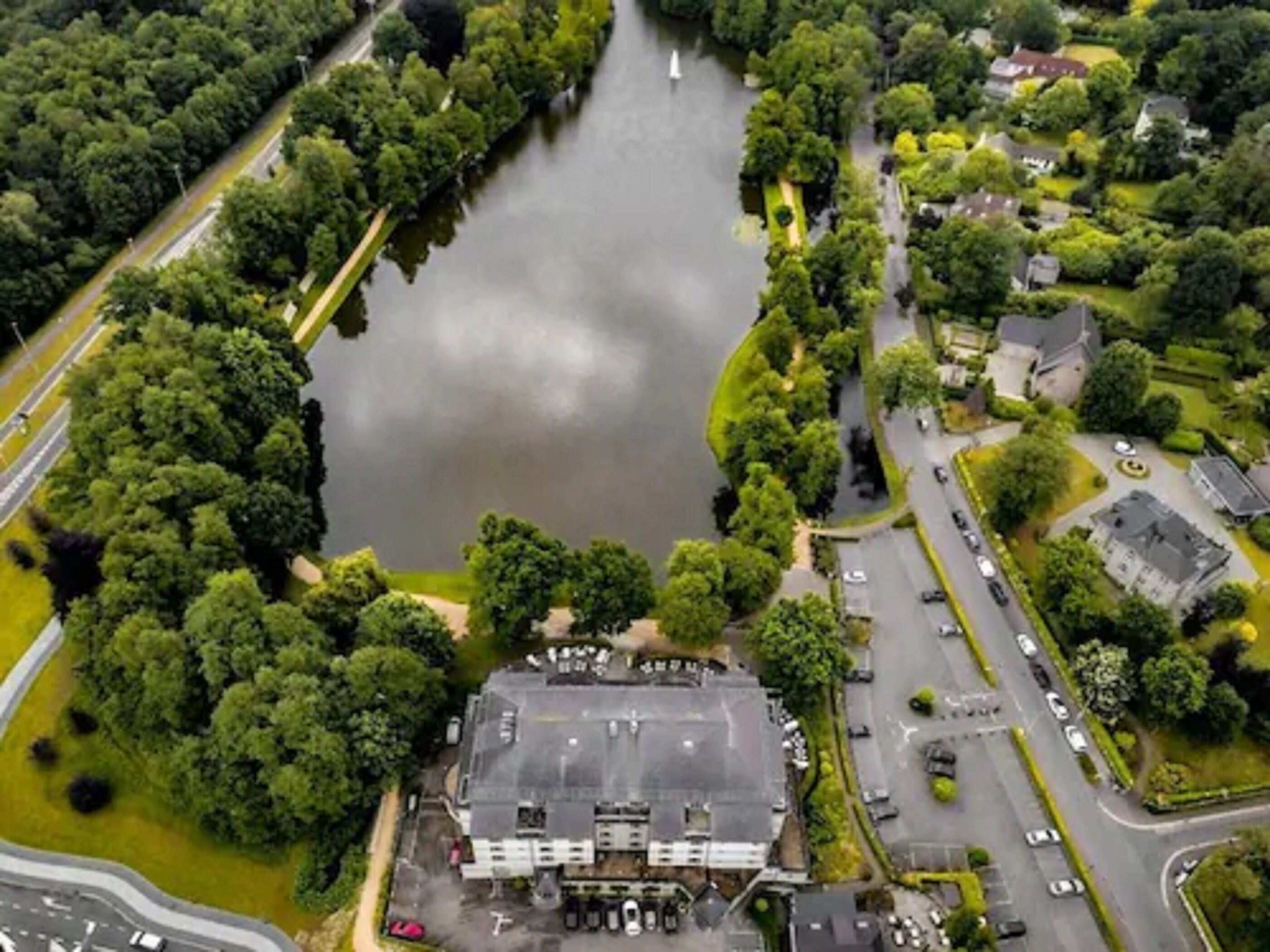 Luchtbeeld van een gebouw met een parkeerplaats, omringd door groen en water.