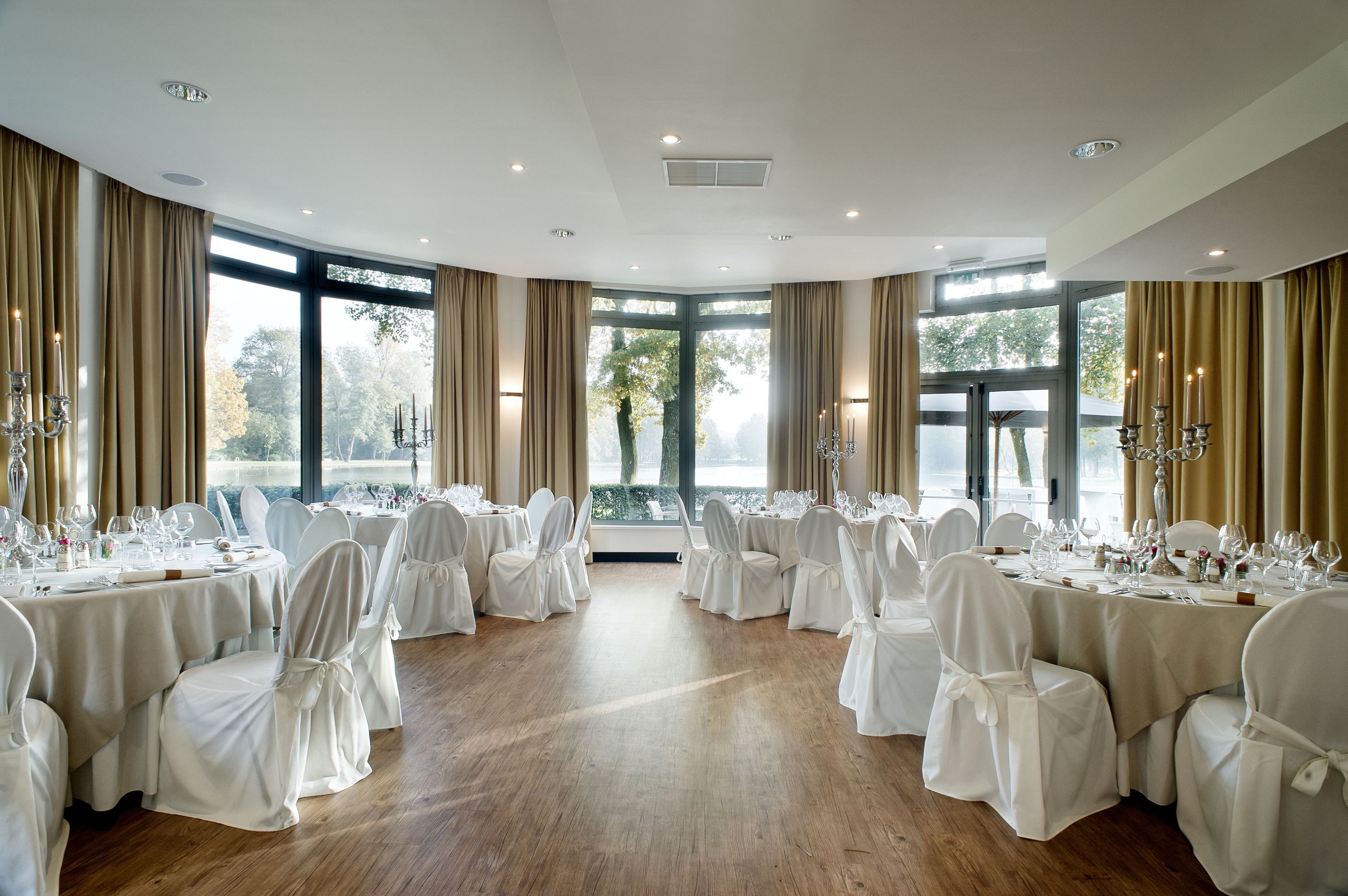 A banquet hall with round tables set for dining, large windows, and chandeliers.