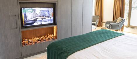 Habitación de hotel con una cama grande, televisor en mueble, chimenea y vistas al exterior.