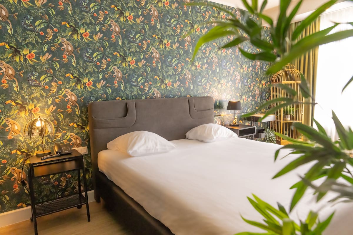 A neatly made bed with white linens, a dark grey headboard, and a small bedside table with a lamp and a phone.