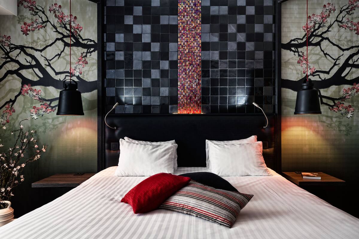 A modern bedroom with a large bed, two bedside tables, and a wall with a tree mural.
