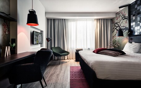 A modern hotel room with a bed, desk, chair, and a large window with curtains.