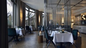 A modern restaurant with tables set for dining, large windows, and a view of trees outside.