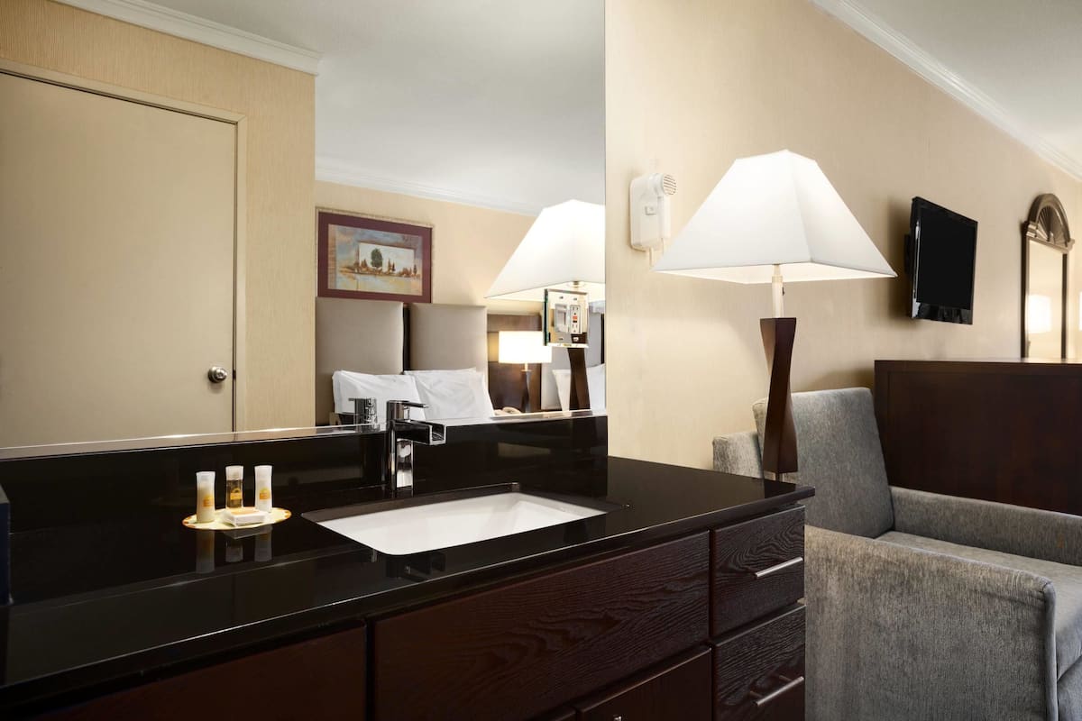 A hotel bathroom with a black countertop, a sink, a mirror, a towel rack, and a chair.