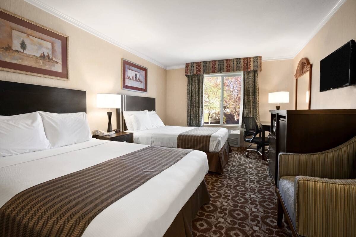 A hotel room with two beds, a desk, a chair, a TV, and a window with curtains.