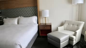 Hotellihuone, jossa on sänky, yöpöytä, lamppu, tuoli ja rahi.