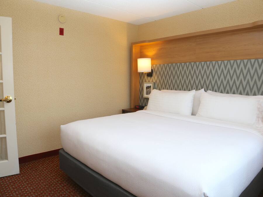 Una habitación de hotel con cama, mesita de noche, lámpara y puerta.