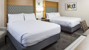 A hotel room with two beds, a desk, a chair, a lamp, and artwork on the walls.