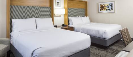 A hotel room with two beds, a desk, a chair, a lamp, and artwork on the walls.