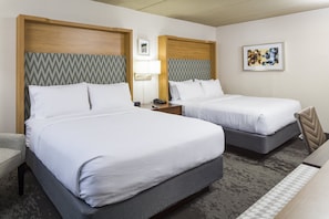 Une chambre d’hôtel avec deux lits, un bureau, une chaise, une lampe et des œuvres d’art accrochées aux murs.