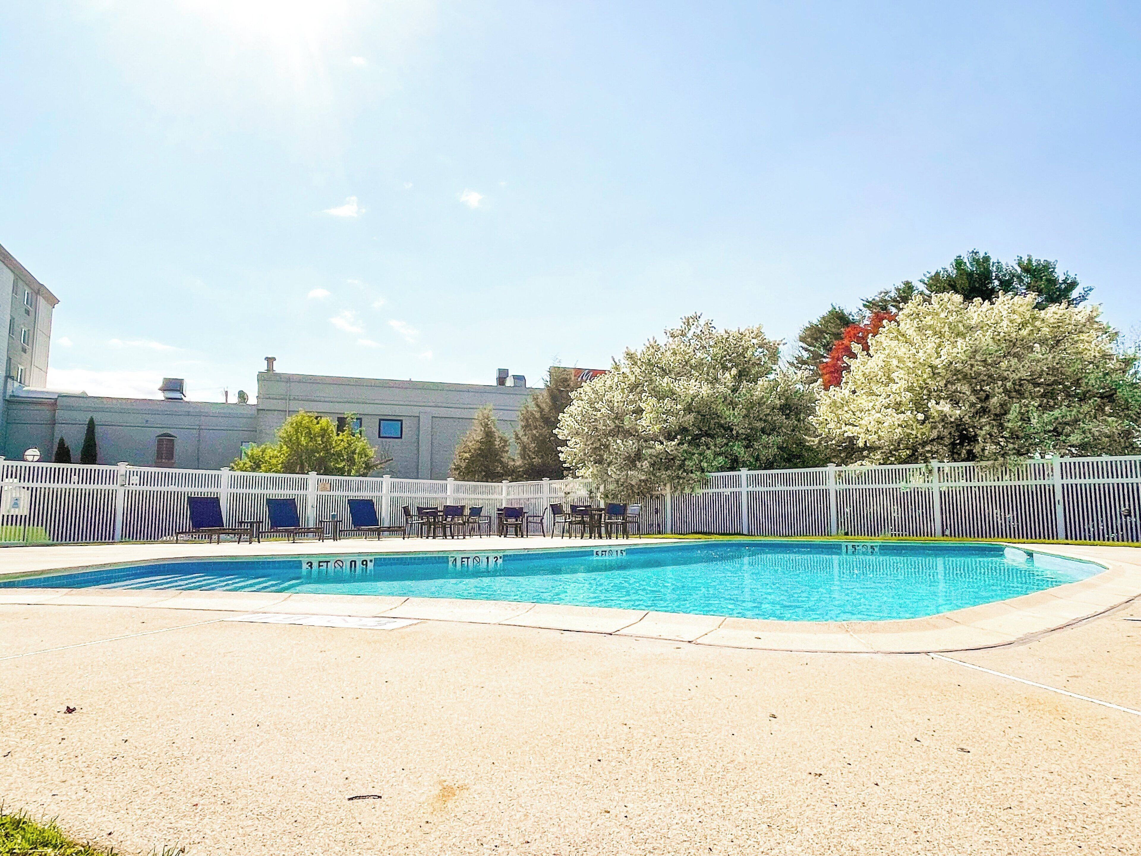 Una piscina amb gandules i una tanca, envoltada d'arbres i edificis.
