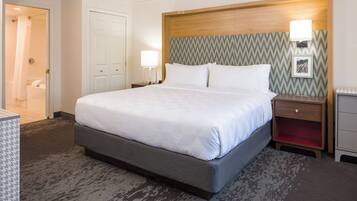 A hotel room with a large bed, bedside tables, a nightstand, a wooden headboard, and a patterned wall.