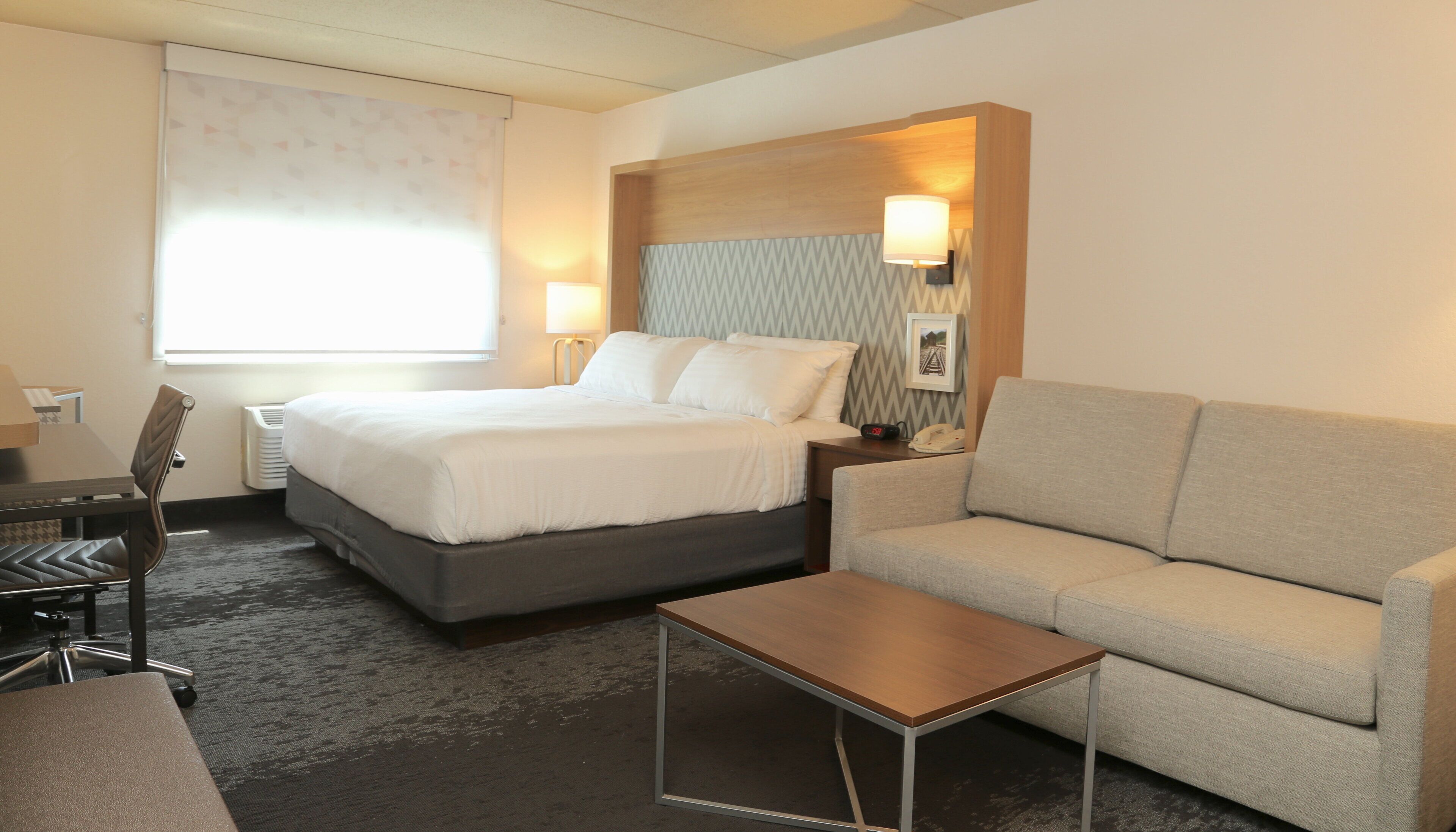 A hotel room with a bed, a sofa, a small table, a desk, and a chair.