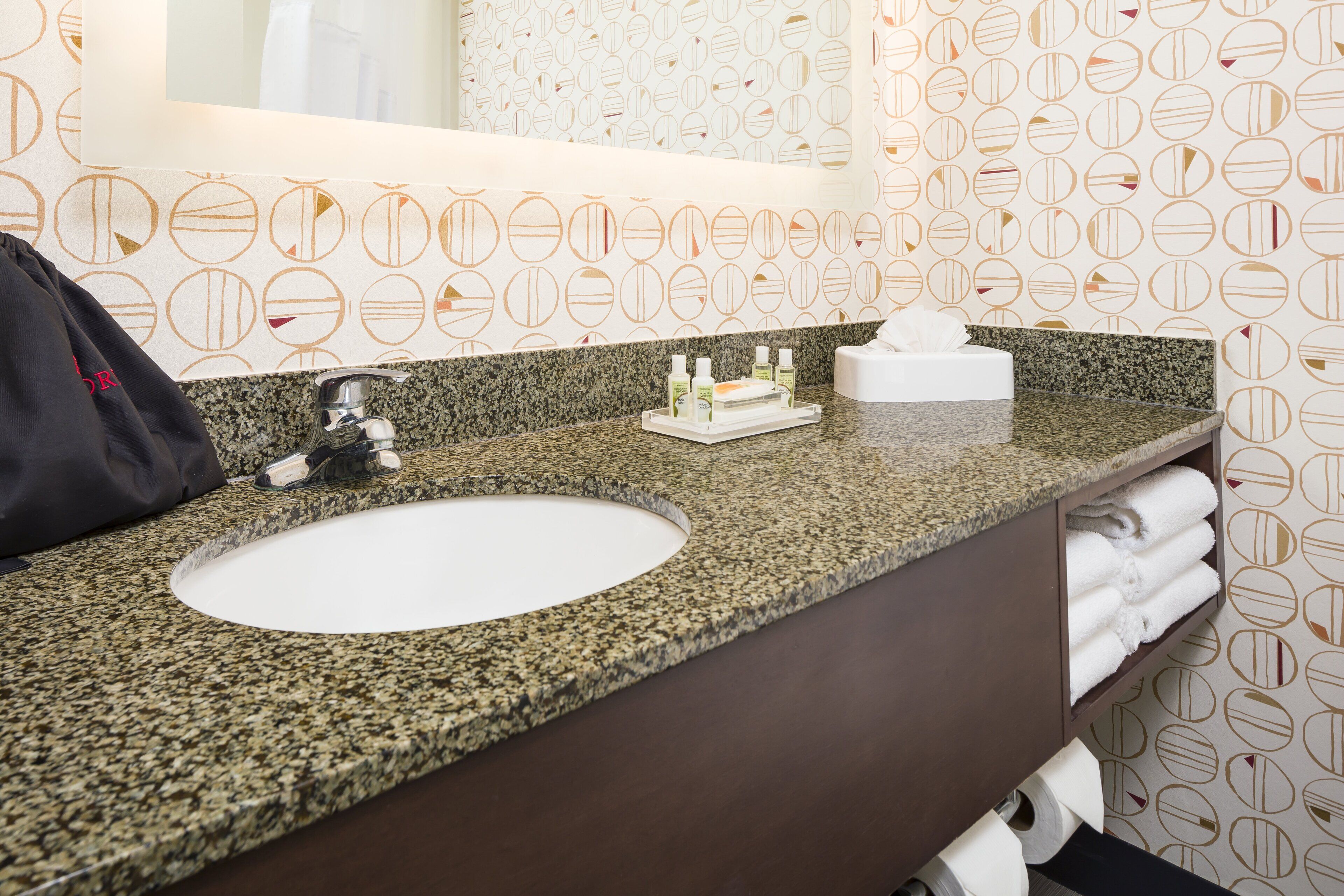 A bathroom with a granite countertop, a white sink, a mirror, and a towel rack with folded towels.