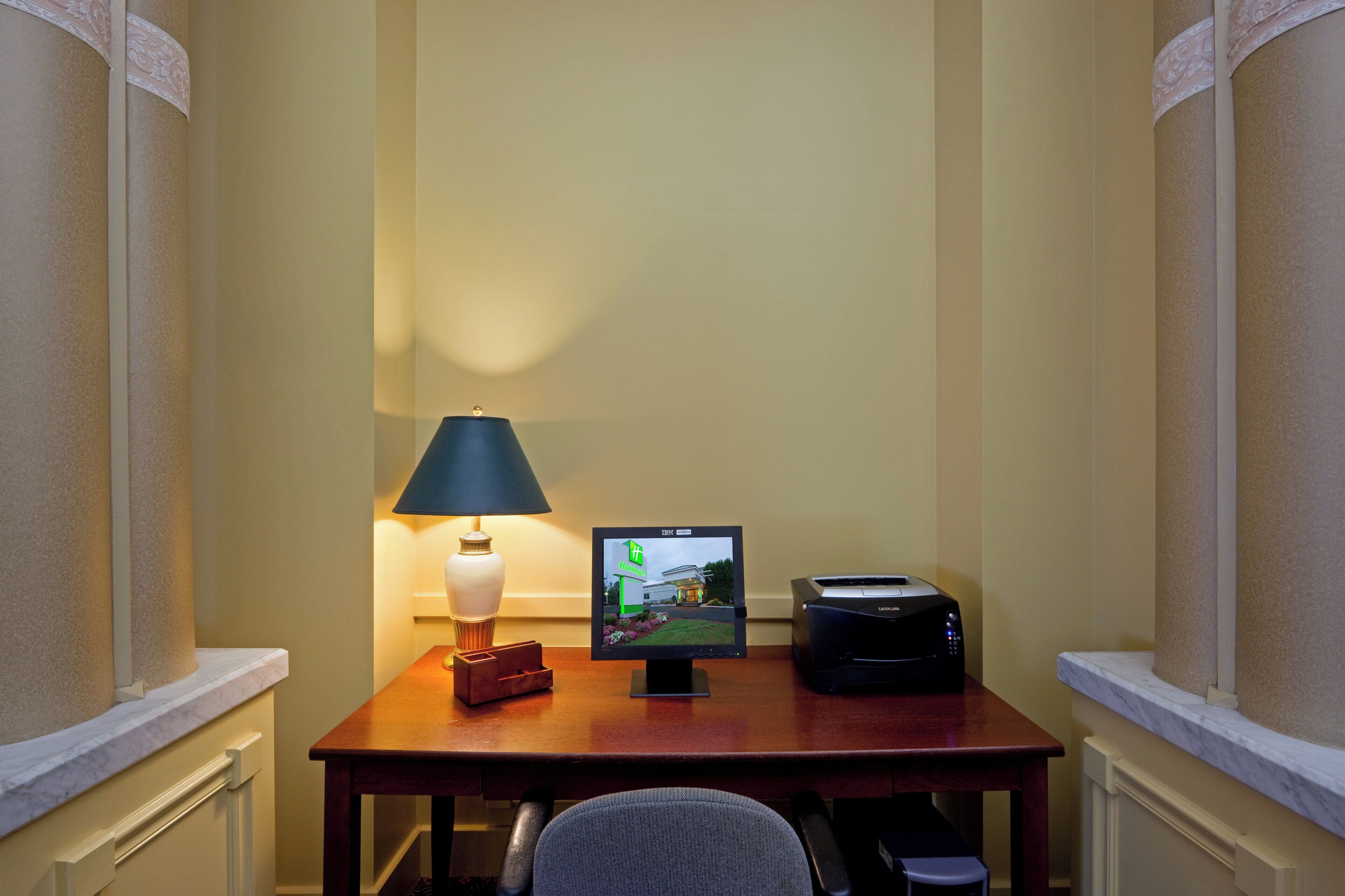 A hotel room with a desk, a lamp, a television, and a printer.