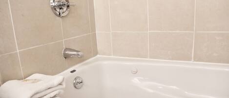 A white bathtub with a towel on the side, a chrome faucet, and a wall-mounted control panel.