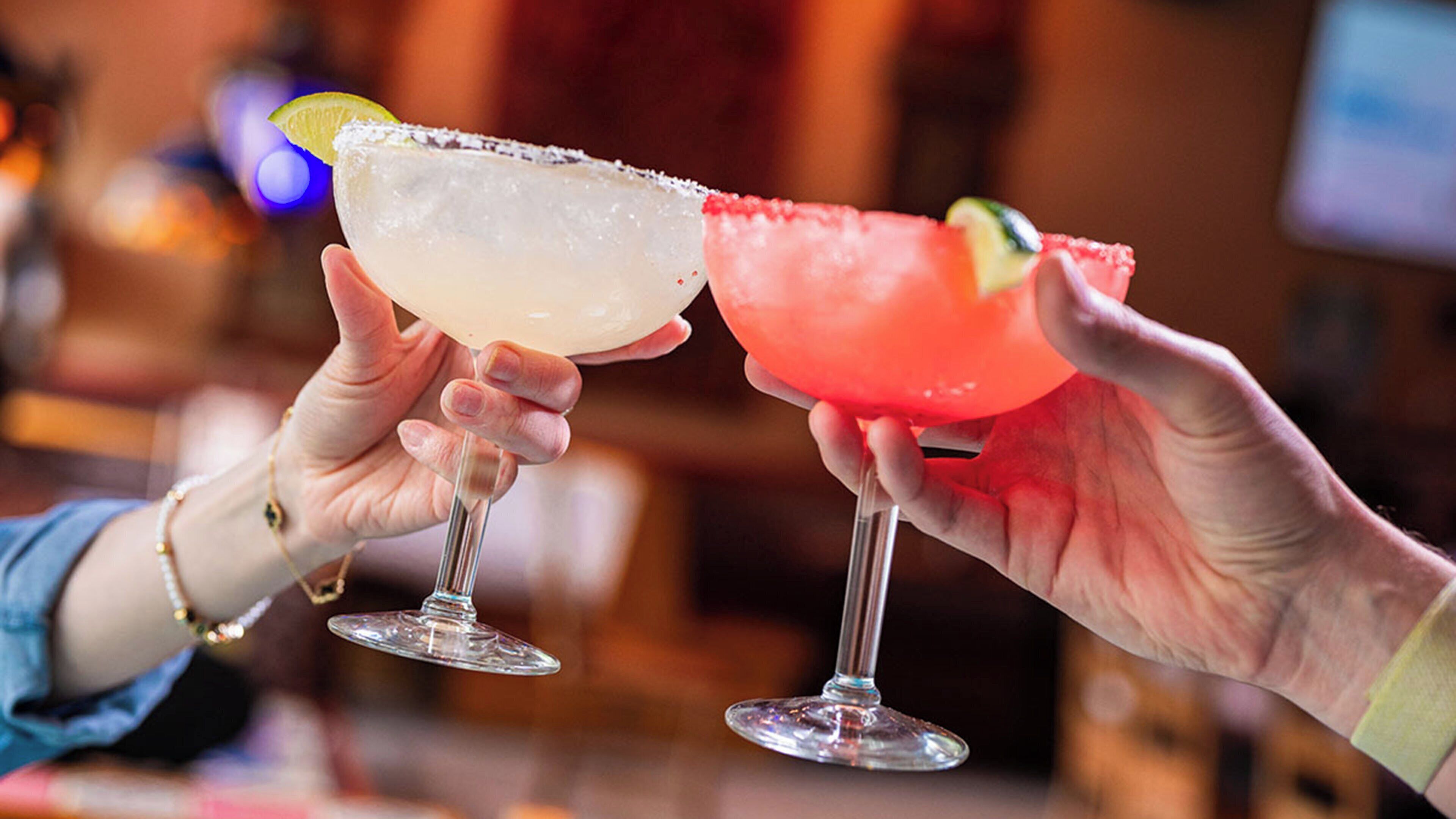 Two hands holding cocktail glasses with a lime garnish.