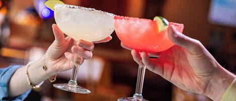 Two hands holding cocktail glasses with a lime garnish.