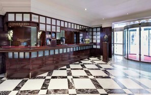 A reception area with a checkered floor, a reception desk labeled 'CONSERJERIA,' and a 'Sercotel hotels' sign. - Sercotel Gran Hotel Conde Duque (Madrid)