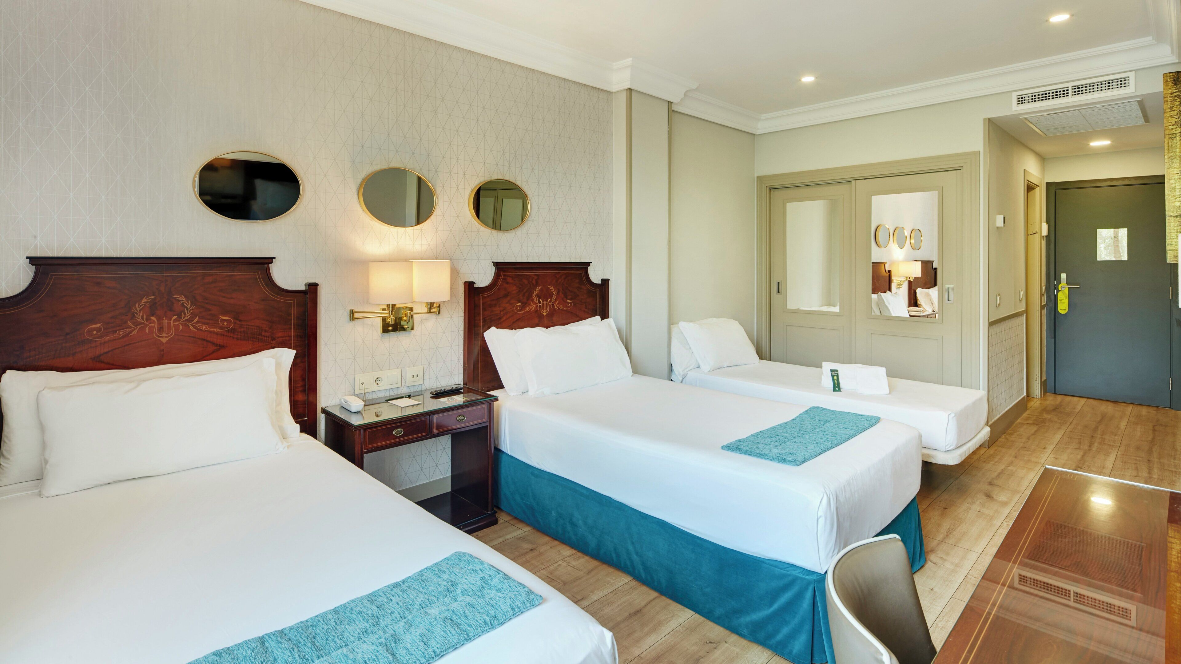 A hotel room with two beds, a desk, a mirror, and a door.