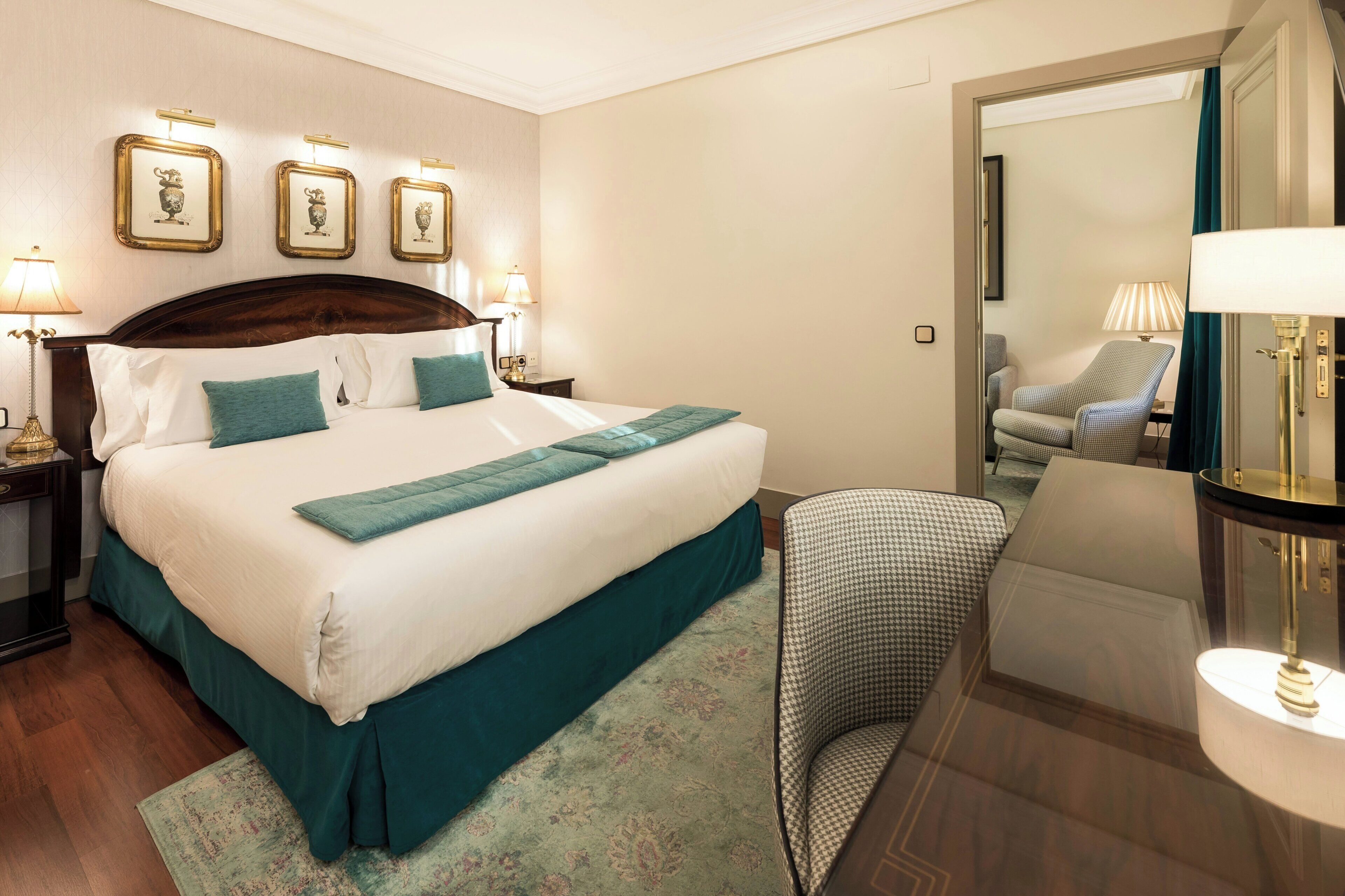 Een hotelkamer met een groot bed, een stoel, een lamp en lijstwerken aan de muur.