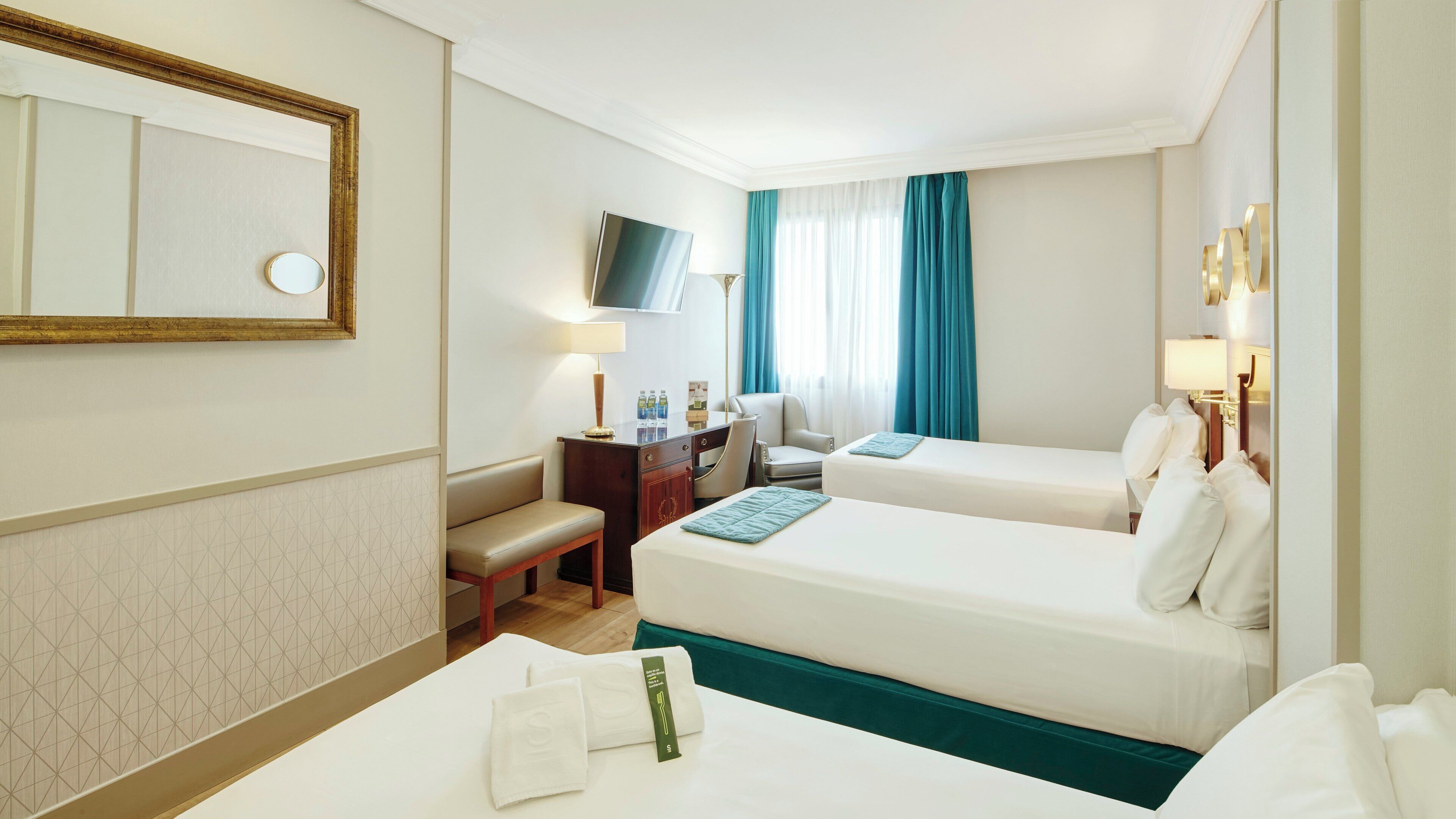 A hotel room with two beds, a desk, a chair, a TV, and a mirror.