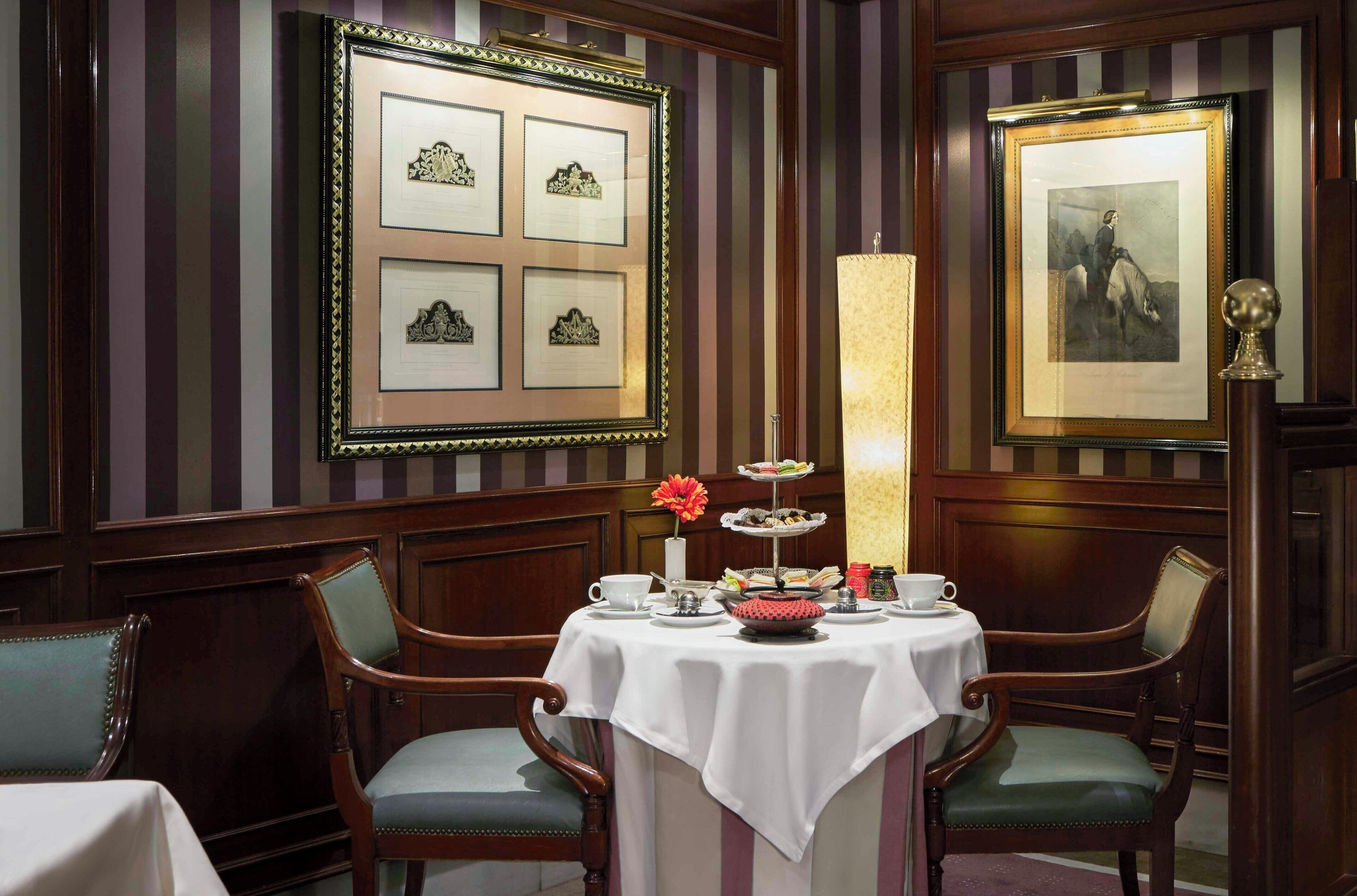 Un comedor con una mesa preparada para dos, una obra de arte enmarcada en la pared y una lámpara alta y cilíndrica.