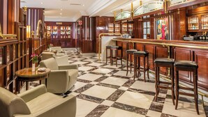 A bar area with wooden bar stools, a checkered floor, and a bar counter with glassware. - Sercotel Gran Hotel Conde Duque (Madrid)