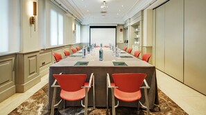 A conference room with a long table, red chairs, water bottles, and a projector screen at the end. - Sercotel Gran Hotel Conde Duque (Madrid)