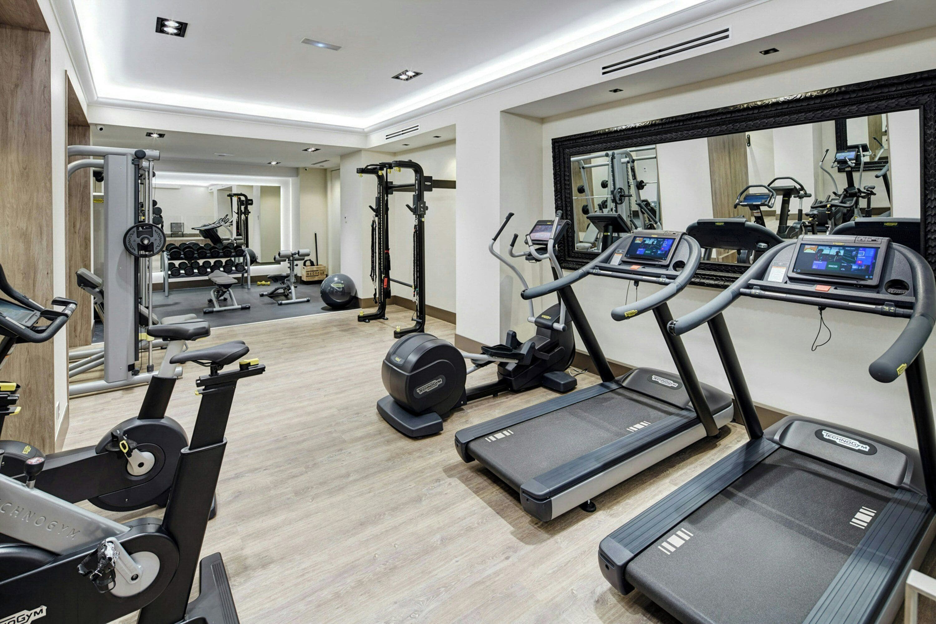 Ein Fitnessstudio mit Laufbändern, Kraftgeräten und einem Spiegel.