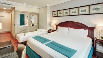 A hotel room with two beds, a desk, a chair, a wardrobe, and framed pictures on the wall.