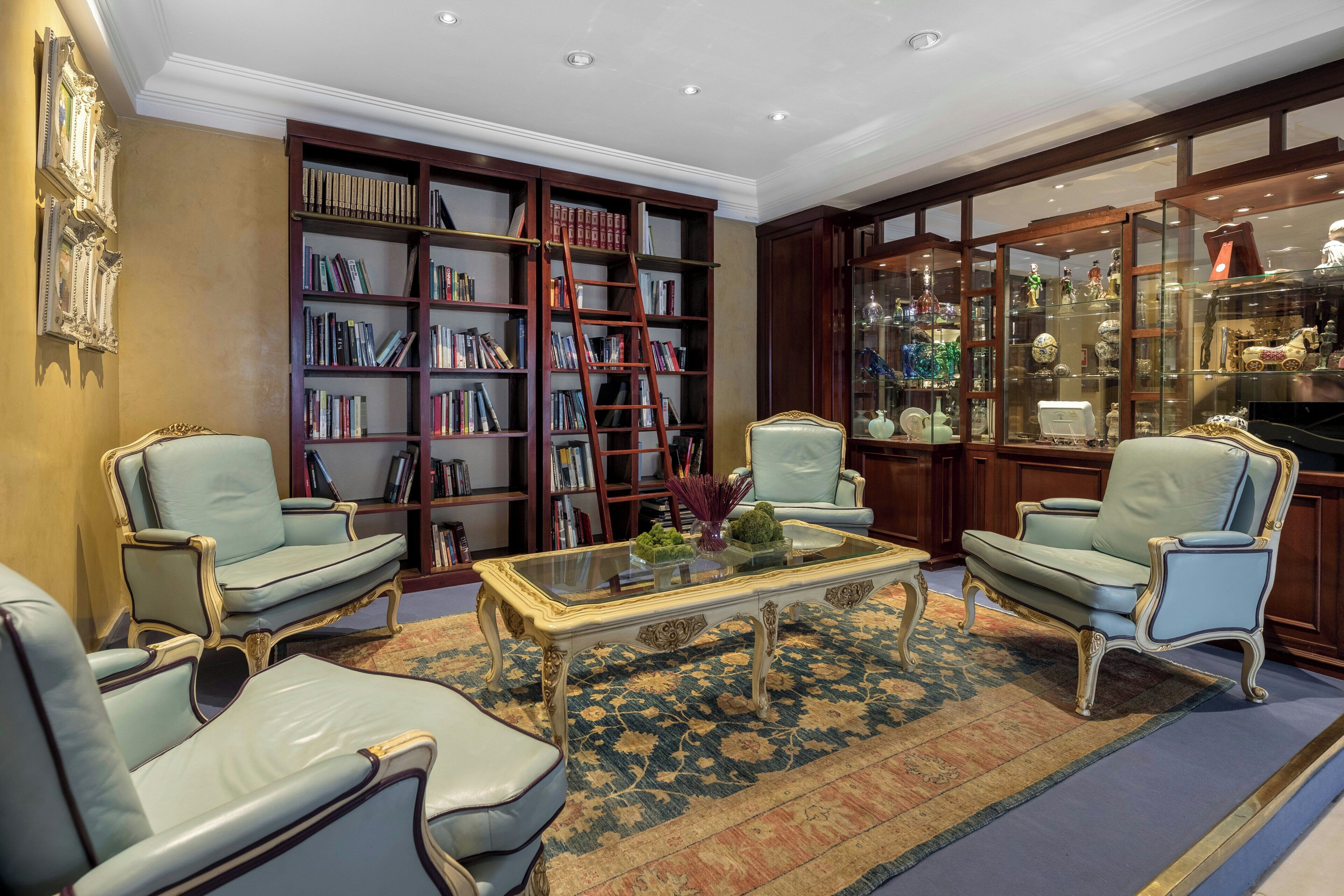 Una habitación con una gran estantería, dos sillones, una mesa de centro y una vitrina de cristal.