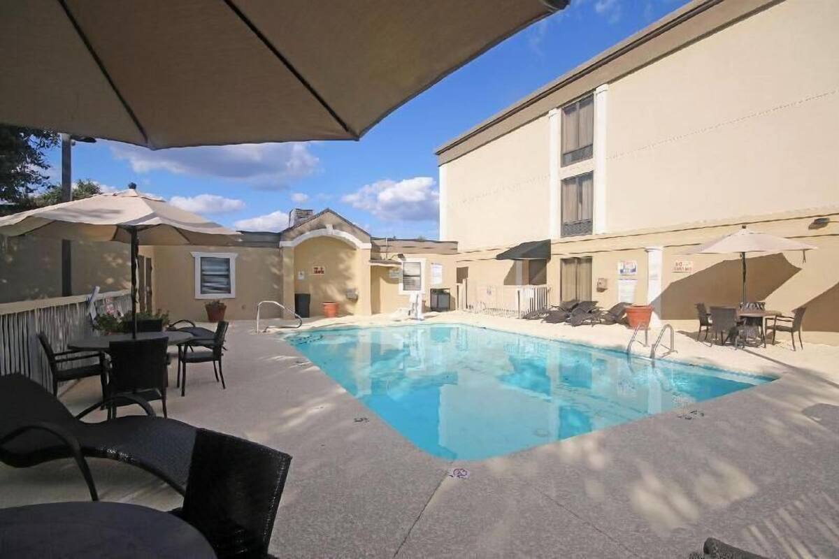 Une piscine avec des chaises longues et des parasols, un bâtiment à la façade beige et un ciel dégagé.