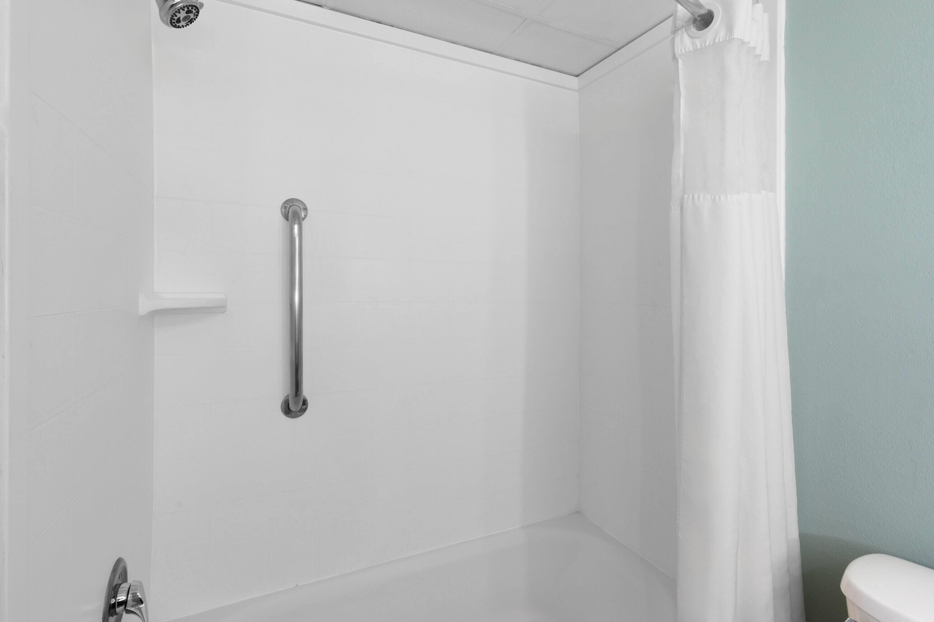 Rincón de un baño con box de ducha blanco, barra de apoyo y un inodoro.