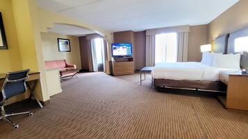 Een hotelkamer met een bed, een bureau met stoel, een televisie en een raam met gordijnen.